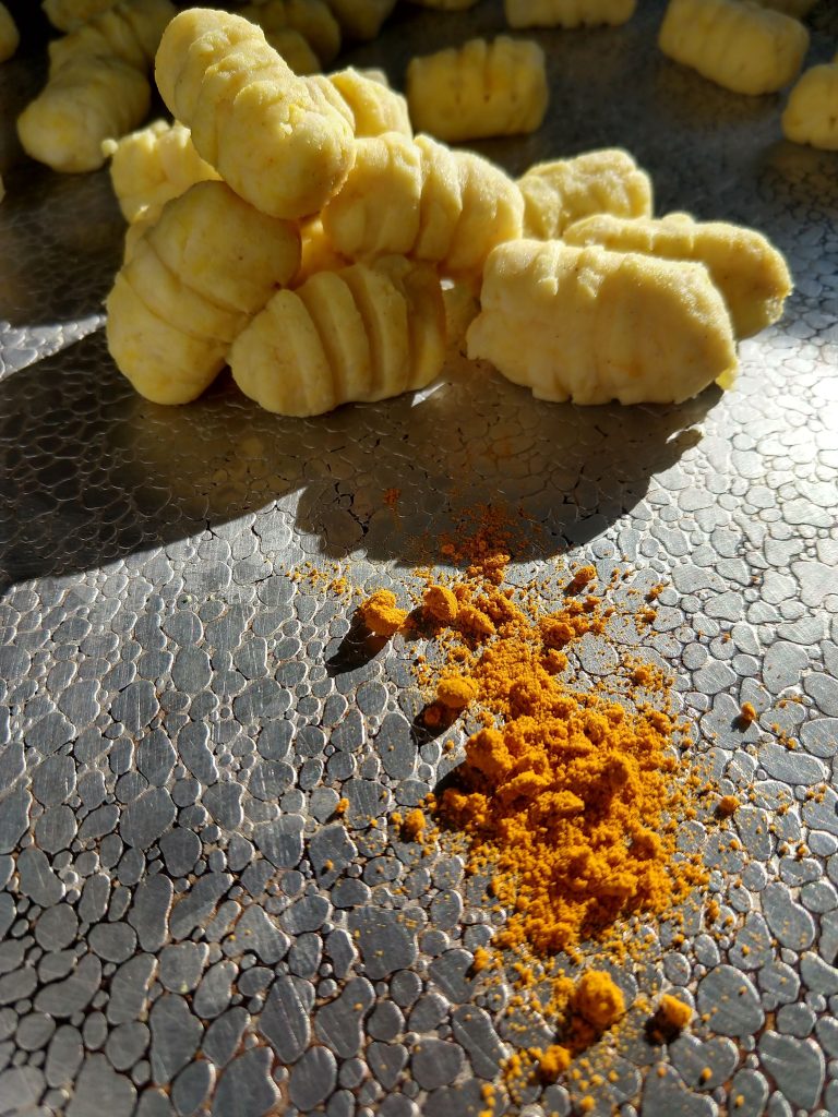A pile of easy to chew turmeric mashed potato gnocchi are displayed on a metallic plate with a sprinkle of turmeric in the foreground.