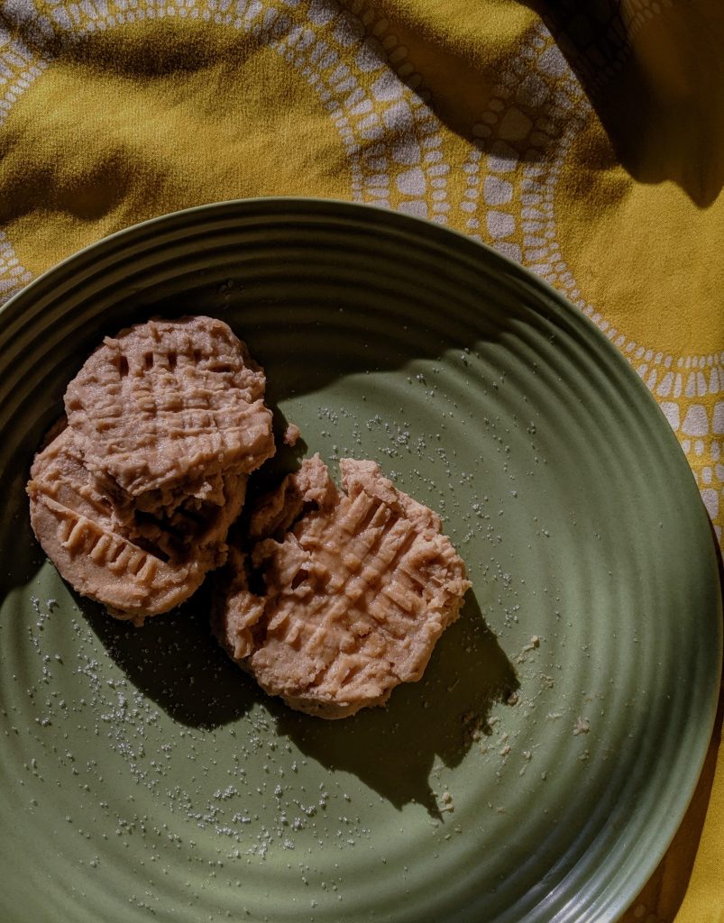 Pureed Peanut Butter Chickpea Cookie Dough is plated on a green plate on a yellow background in round shapes that have crosshatching on top and are sprinkled with salt and sugar