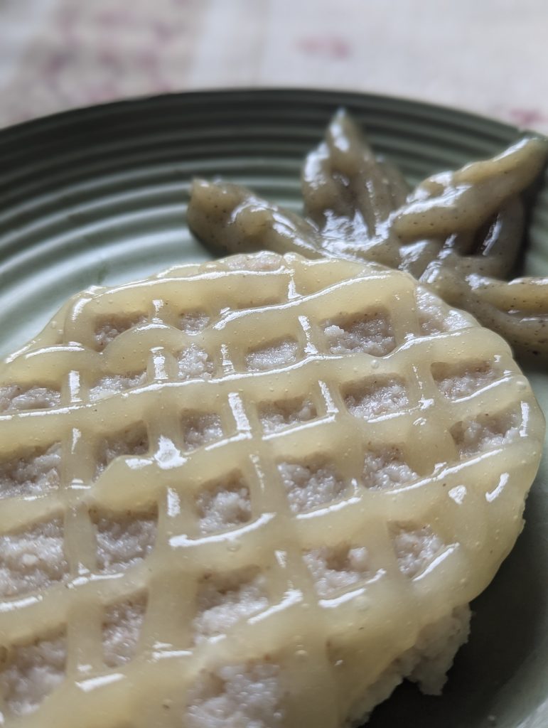 An oval of cream of wheat cereal is centered on a green plate with a grid of pineapple puree creates the texture of the fruits skin on top, with a kiwi puree piped in for the leaves of the fruit.