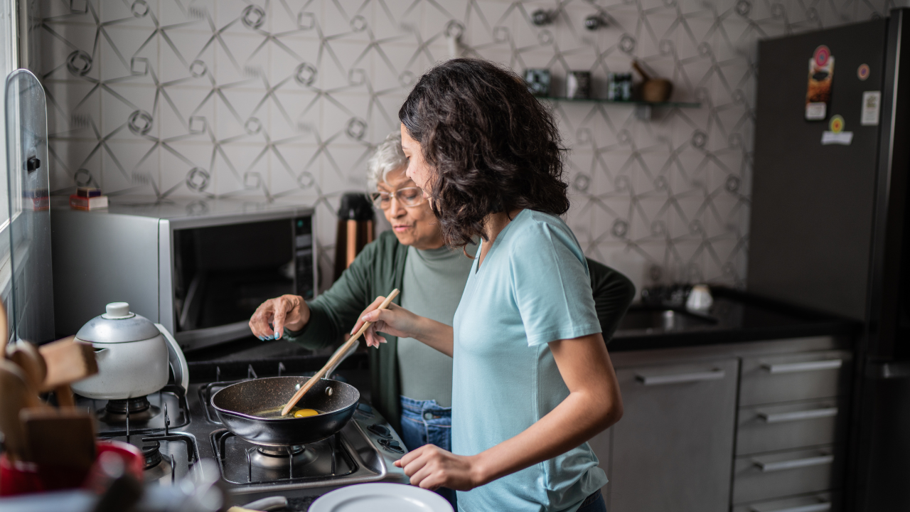 A grandmother directs her granddaughter as she stirs a pan at the stove