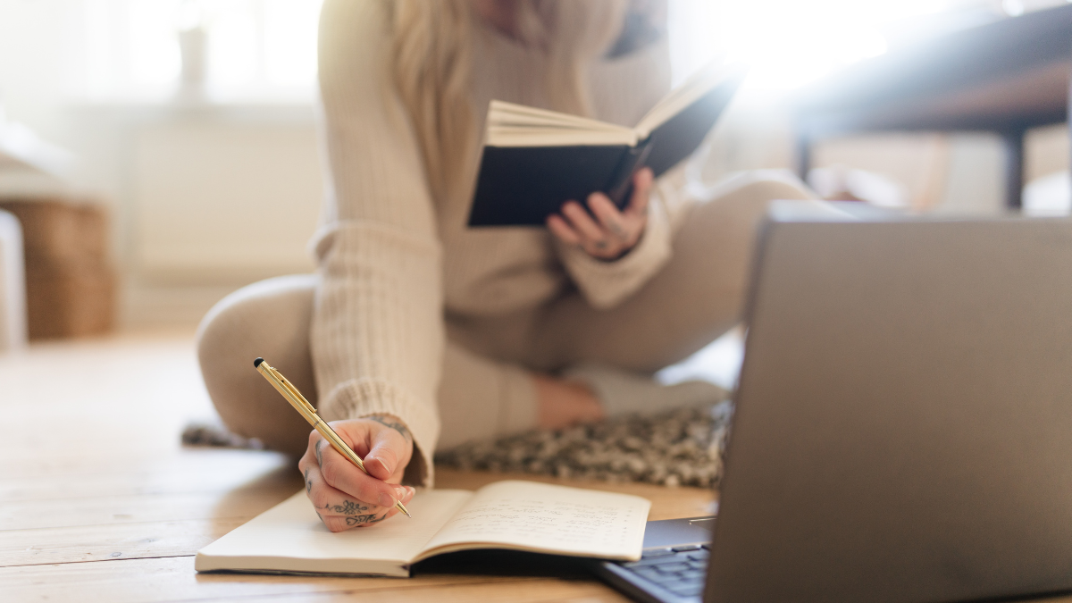 Woman researching with a book and laptop, taking notes