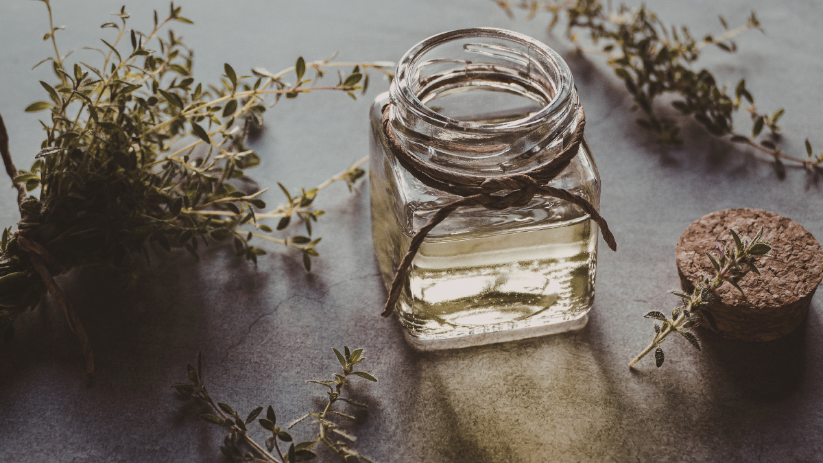 Herbs and a jar of infused oil on a cutting board